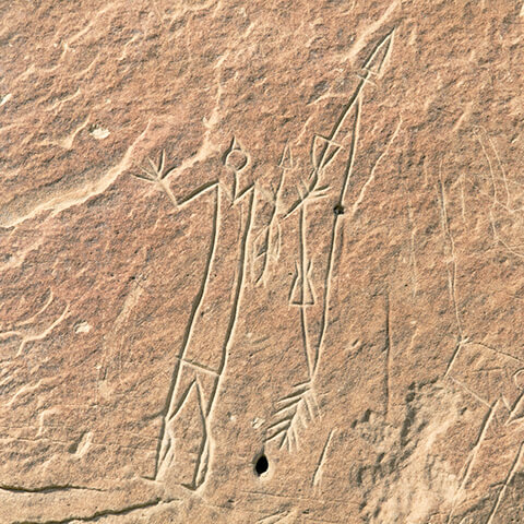 Gravure d'une figure humaine avec un corps rectangulaire et des bras levés. À ses côtés, il y a un arc et des flèches.
