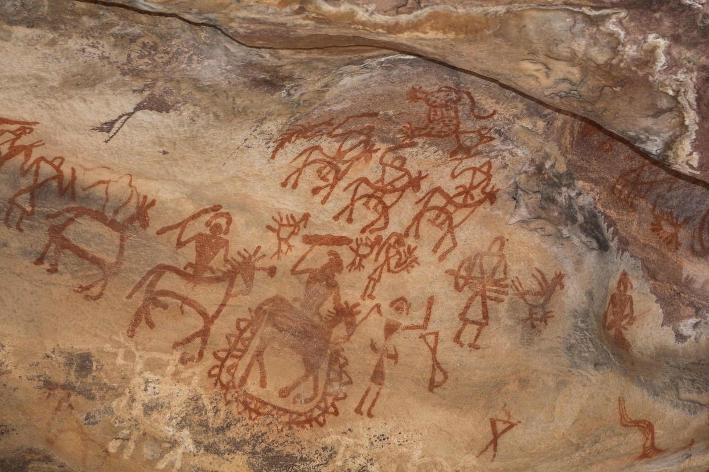 Photographie d'une peinture rupestre localisée à Bhimbetka en Inde. Scène représentant des hommes à cheval et à pied, revenant de guerre ou d'une chasse collective.