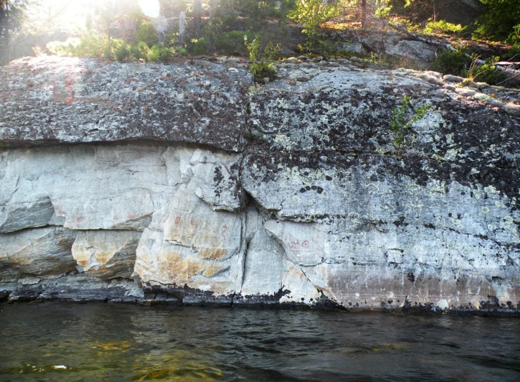 Picture of the Diamond Lake site, in Ontario, Canada. A horned snake, canoes and a bird track are painted on a rock outcrop.