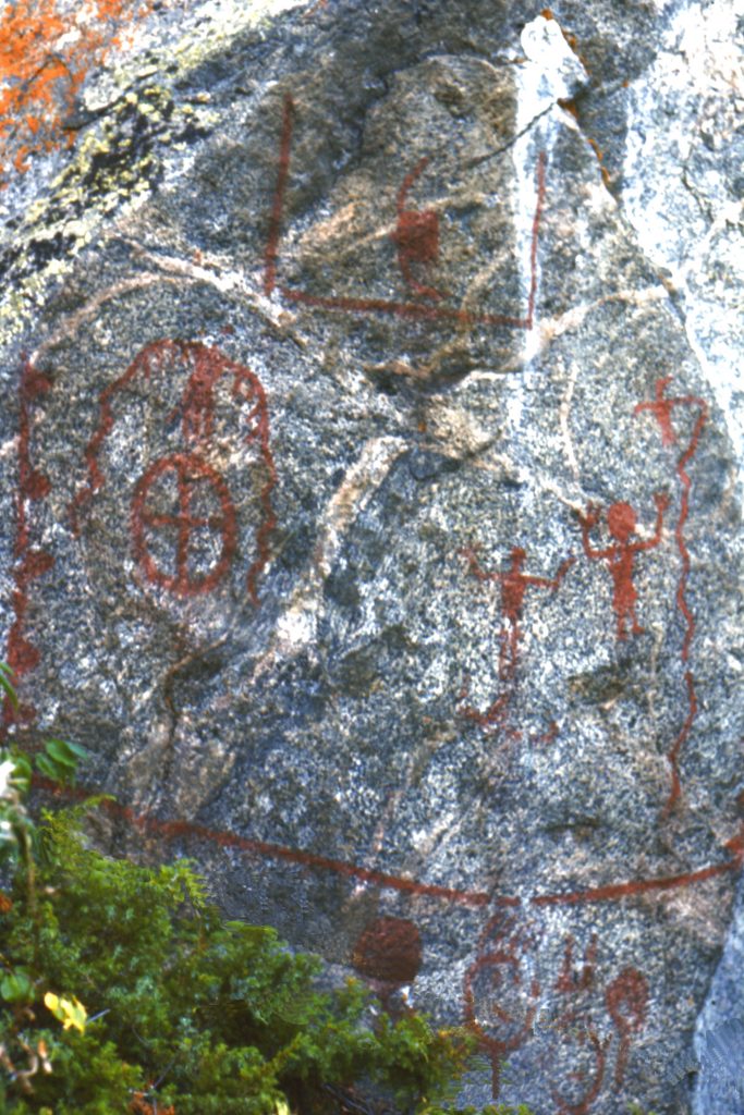 High Rock Narrows, Saskatchewan. Image représentant plusieurs peintures rupestres, dont un oiseau avec des longues ailes sinueuses, deux anthropomorphes avec des bras levés et un cercle avec une croix à l’intérieur.