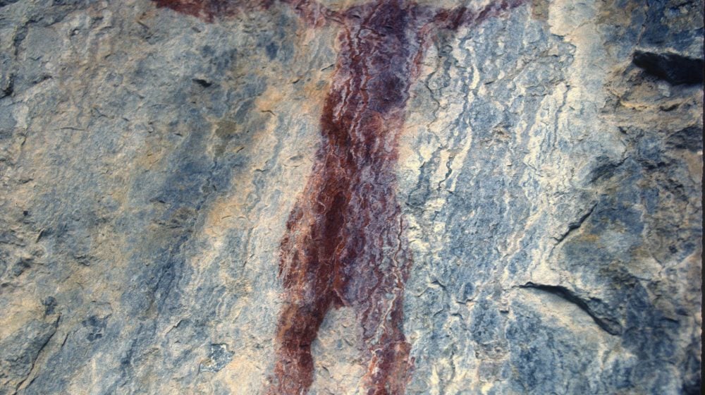Photographie d'une peinture rupestre à Grassi Lake en Alberta. On y voit une figure humaine qui tient un objet circulaire : un cerceau, un tambour ou peut-être un bouclier.
