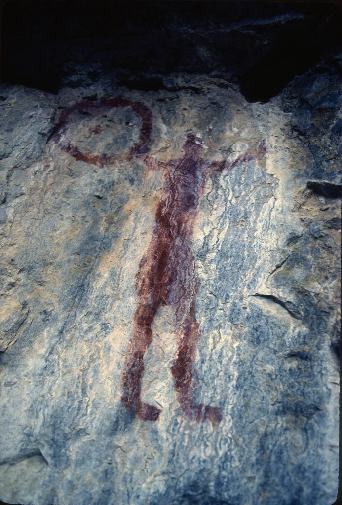 Photograph of a rock painting at Grassi Lake, Alberta. It represents a human figure holding a circular object: a hoop, a drum or maybe a shield.