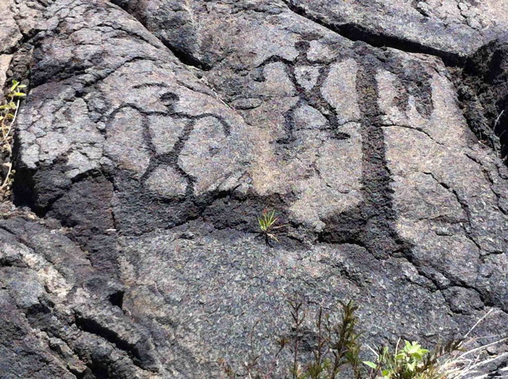 Photographie d'une représentation anthropomorphe composée de deux personnages gravés dans la pierre. Site du parc national des Volcans, Hawaï, États-Unis d’Amérique.